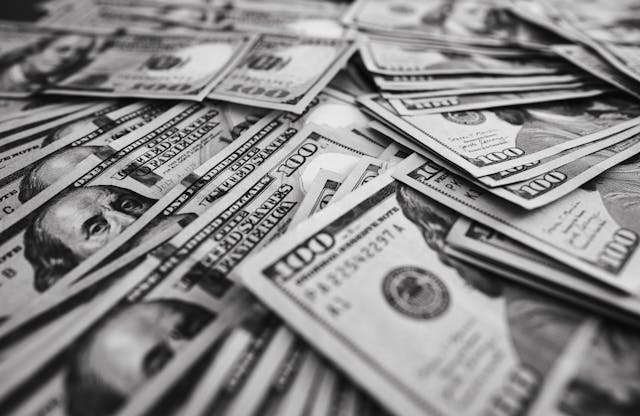 A imagem é ilustrativa e mostra várias notas de dólar empilhadas.